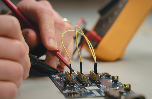 Close-up of multimeter probes testing pin headers on a development board