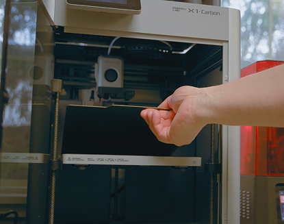 Engineer removing a part from a Bambu Lab X1-Carbon 3D printer